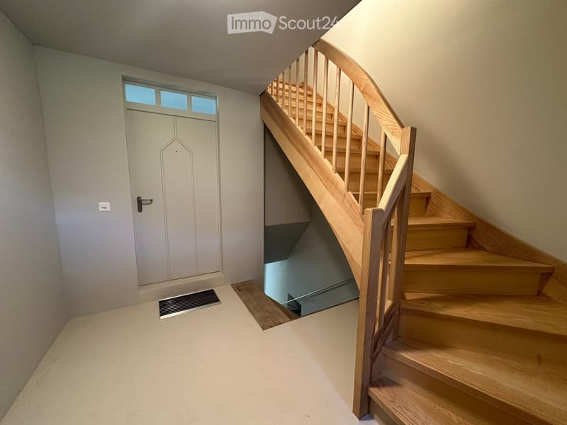 Spacious hallway with a wooden staircase leading upwards, a door with frosted glass panels, and a small vent on the floor.