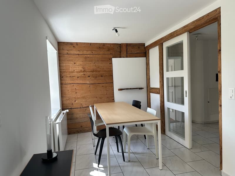 Modern dining area with a wooden table, white and black chairs, radiator, and a wooden accent wall.