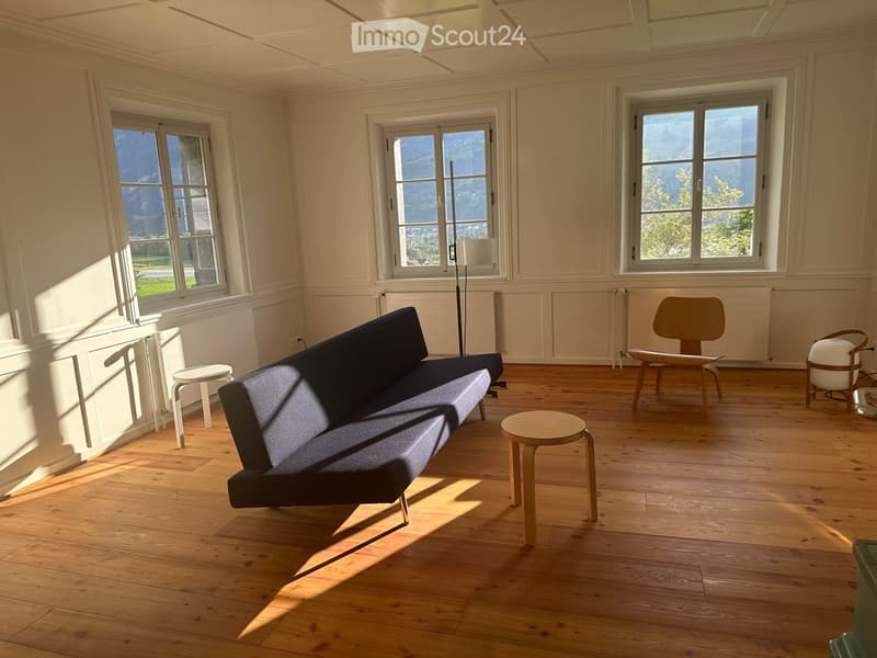 Bright living room with wooden flooring, large windows offering a scenic mountain view, and modern furniture including a sofa, stools, and a floor lamp.