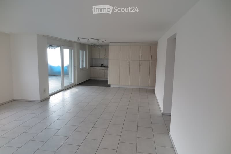 Empty room with tiled floor, white walls, and a sliding glass door leading to another room with kitchen cabinets and appliances.