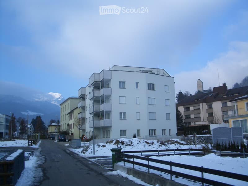 Multi-story residential building with balconies and windows, surrounded by other buildings and a snow-covered landscape.