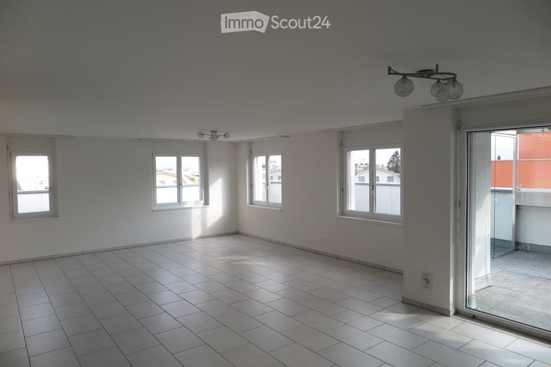 Empty room with tiled floor, white walls, multiple windows, and a sliding glass door leading to a balcony.