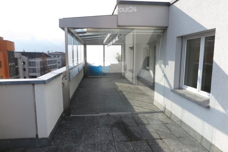 Modern balcony with glass railings, tiled floor, and open views of surrounding buildings.