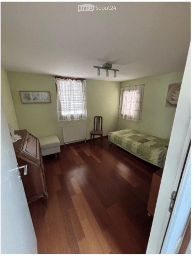 Bedroom with wooden flooring, green walls, a single bed, a wooden chair, a radiator, a dresser, and a small stool.