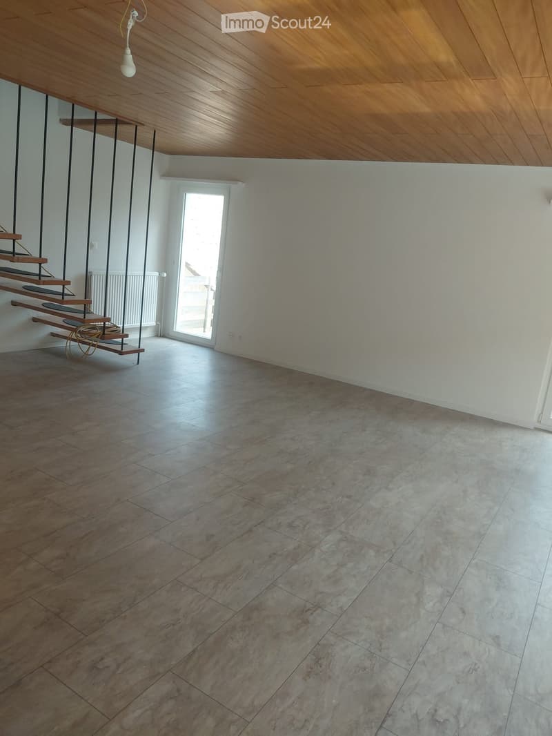 Empty room with wooden ceiling, tiled floor, staircase leading upwards, and a window letting in natural light.