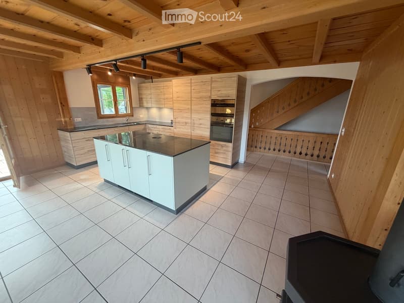 Modern kitchen with light-colored cabinets, a central island, and built-in appliances, featuring exposed wooden beams on the ceiling and tiled flooring.