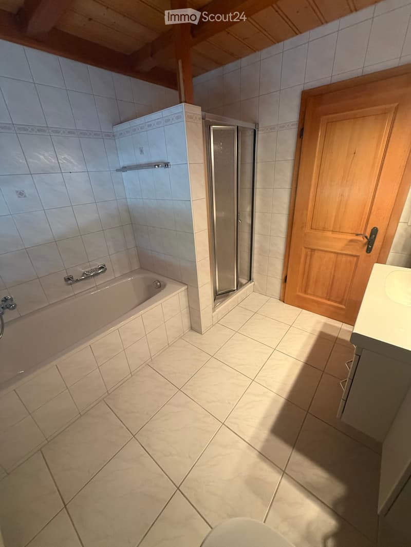 Bathroom with a bathtub, shower, sink, and toilet. The room features tiled walls and floor, wooden door, and a glass shower enclosure.