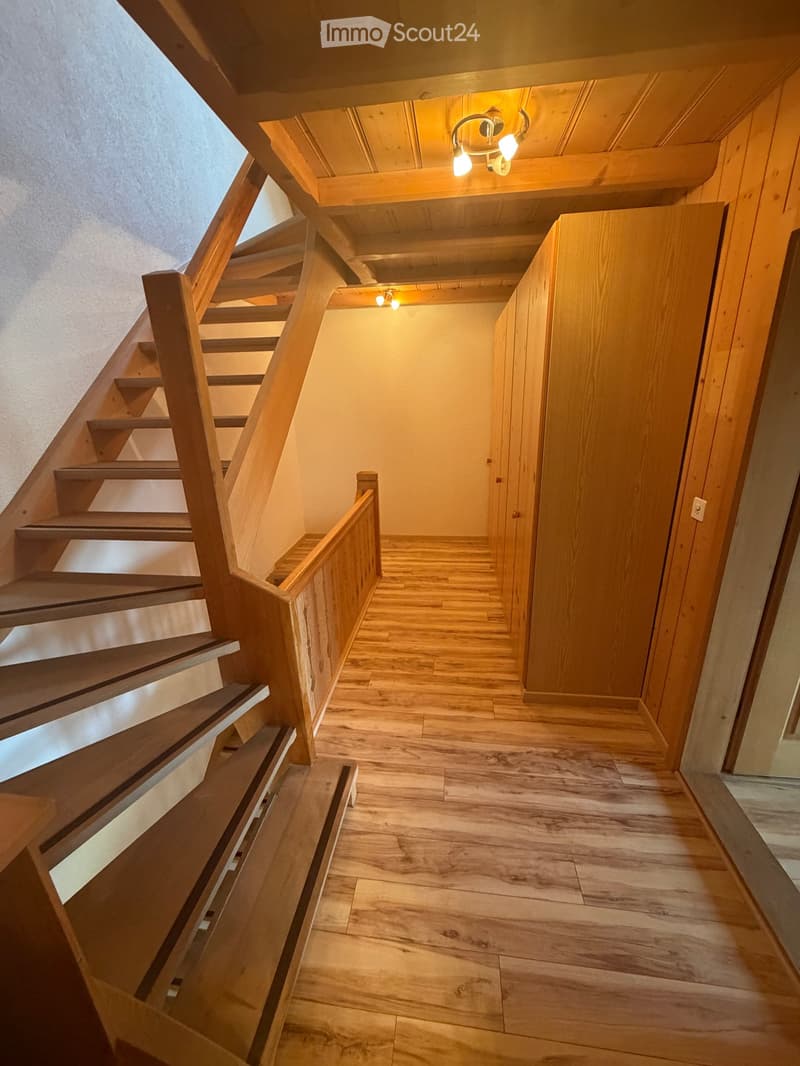 Wooden staircase with a wooden railing and warm lighting, leading to a hallway with wooden flooring and built-in wooden cabinets.