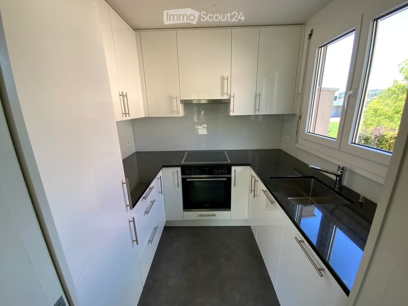 Modern kitchen with white cabinets, black countertops, and stainless steel appliances including a sink, oven, and stove.