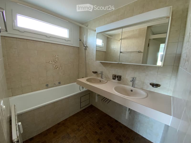Bathroom with a bathtub, double sink, large mirror, and tiled walls.