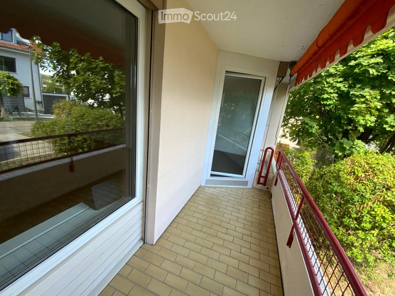 Balcony with tiled floor, glass doors, metal railing, and orange awning.