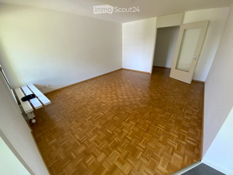 Empty room with wooden herringbone flooring, white walls, and a partially open door leading to another space.