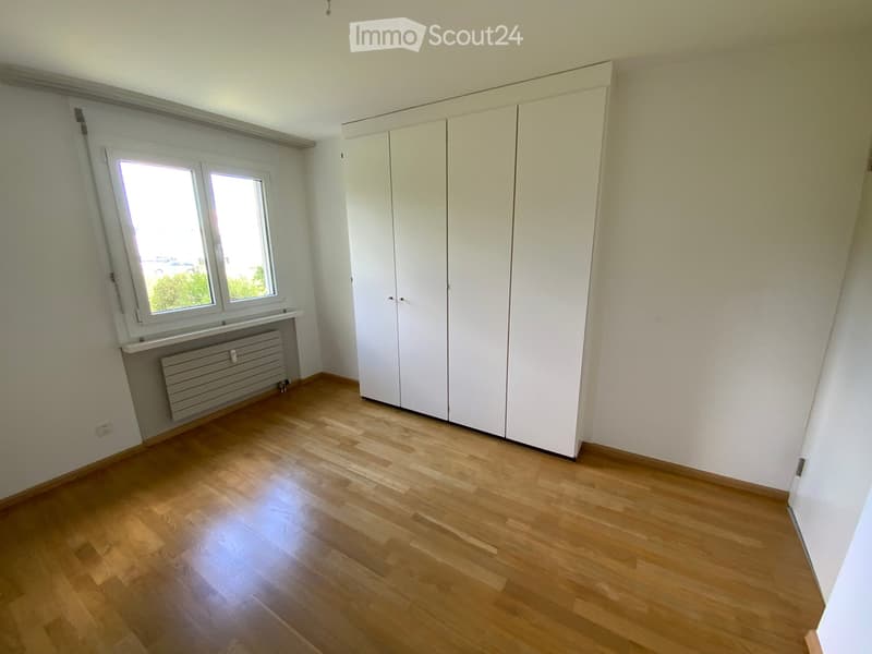 Empty room with wooden flooring, white walls, built-in wardrobes, and a window with blinds.