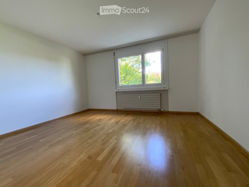 Empty room with wooden flooring, white walls, and a large window with a radiator below it.