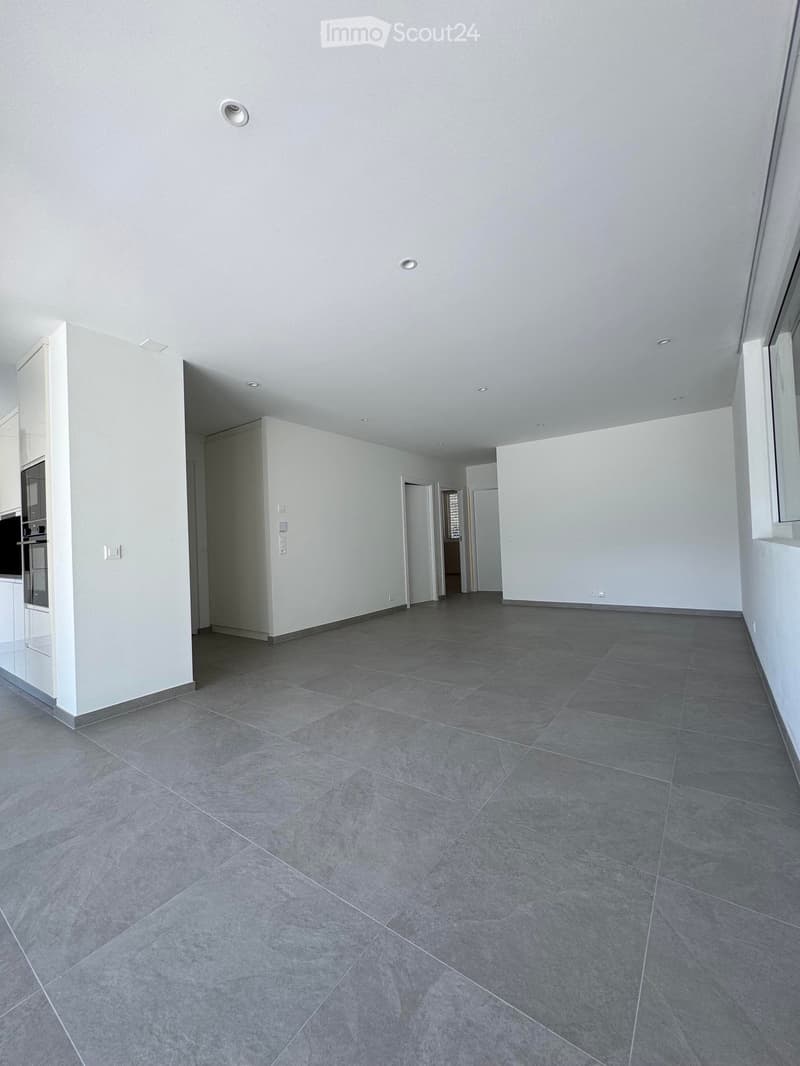 Empty room with grey tiled floor, white walls, and recessed ceiling lights. No furniture or equipment visible.