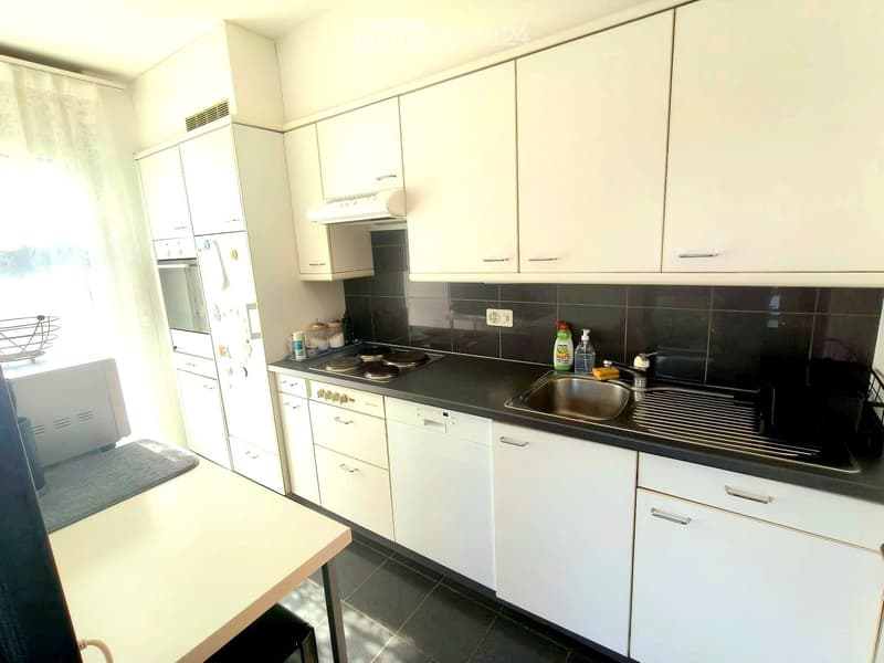 Modern kitchen with white cabinets, stainless steel appliances, and a black countertop. Features include a refrigerator, oven, dishwasher, sink, and various small items on the counter.