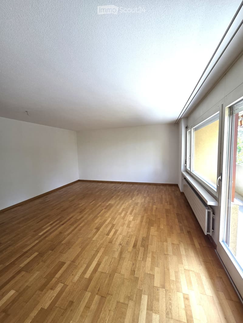 Empty room with wooden flooring and white walls, featuring large windows allowing natural light to enter.