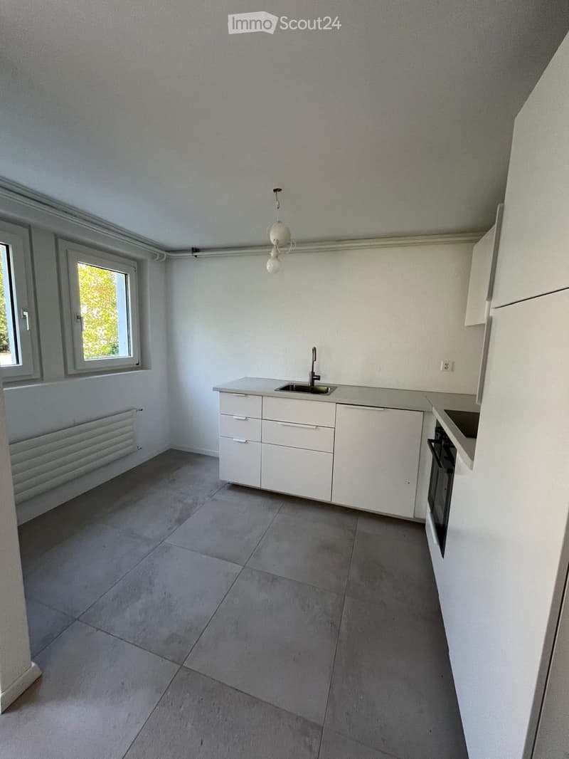 Modern kitchen with white cabinets, a sink, and an oven, featuring a tiled floor and large windows.