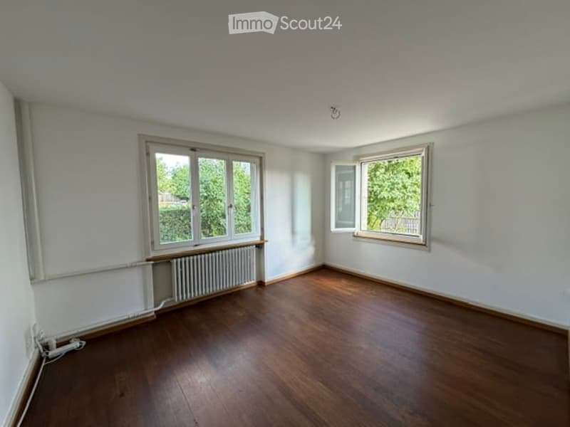 Empty room with wooden flooring, white walls, and large windows with natural light. No furniture or equipment present.