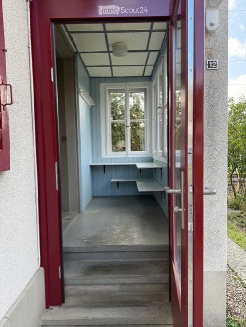 A narrow hallway with a glass ceiling and white walls, leading to a small room with a bench and shelves.