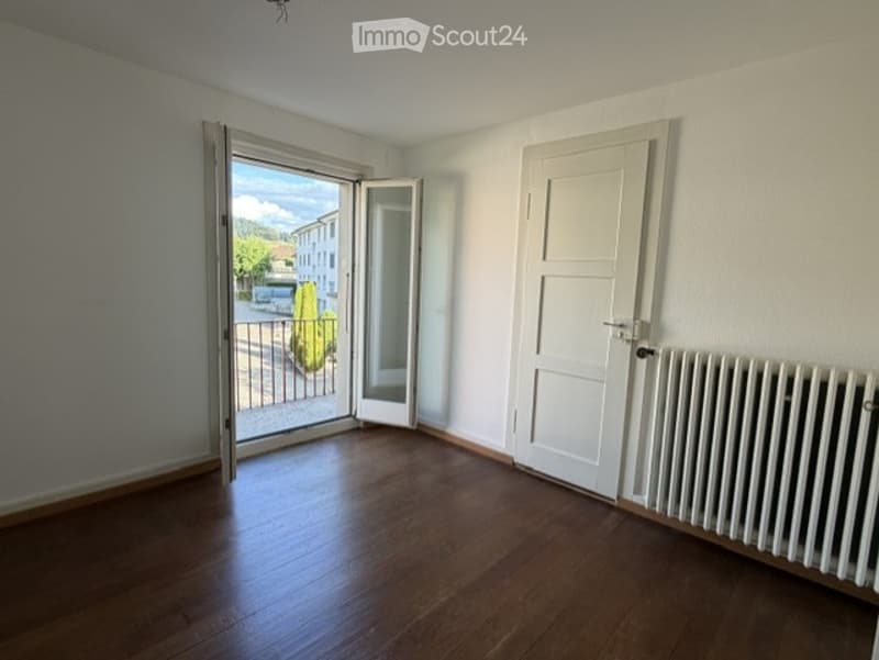 Empty room with wooden flooring, white walls, a white radiator, and a large sliding glass door leading to a balcony or outdoor area.