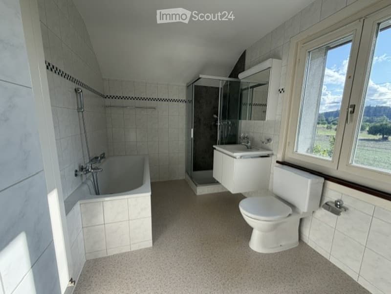 Modern bathroom with white tiles, a bathtub, toilet, sink, and a glass-enclosed shower stall. Large window offers a scenic view.