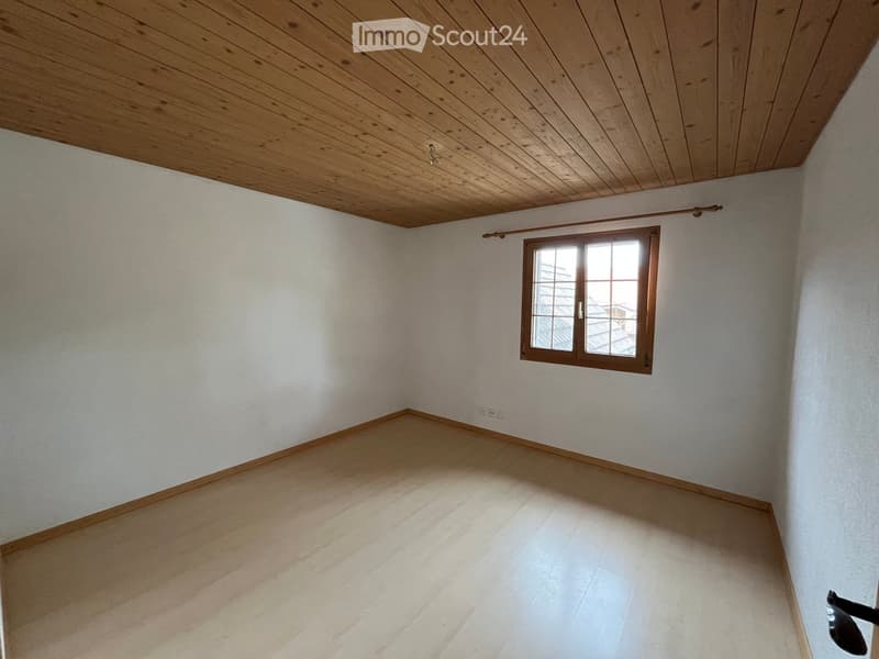 Empty room with wooden ceiling, light-colored walls, and a single window with wooden frame. The floor is covered with light-colored tiles.