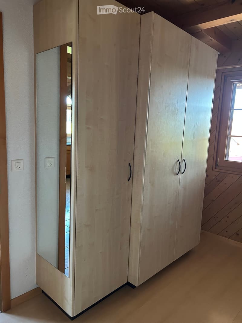 Empty room with light wooden built-in wardrobes, a small window, and a visible electrical outlet on the wall.