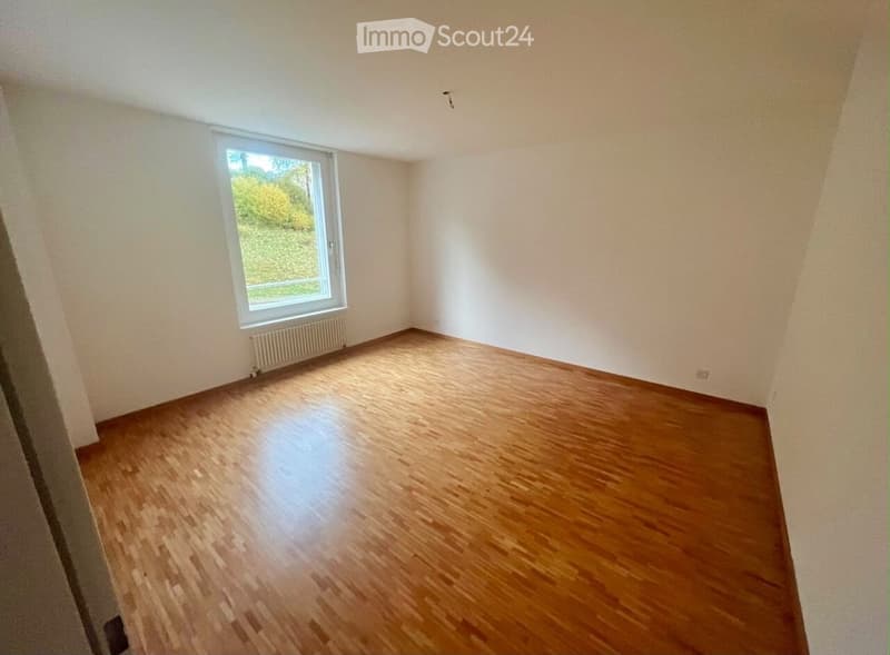 Empty room with wooden flooring, white walls, and a single window with a radiator below it.