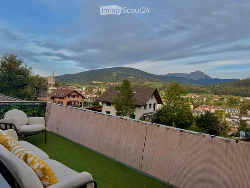 Balcony with artificial grass, white sofa, white armchair, yellow cushions, and a view of a town and mountains.