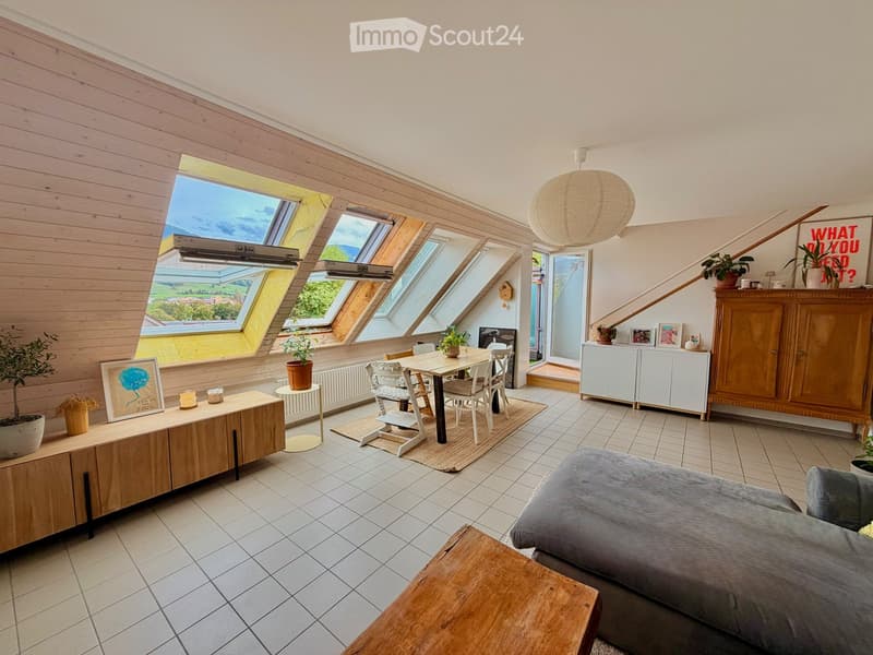 Bright, modern living and dining area with large skylights, a grey sofa, coffee table, dining table with chairs, and wooden cabinets.