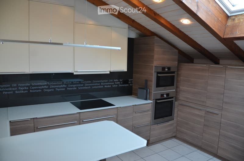 Modern kitchen with light-colored cabinets, wooden accents, induction stove, built-in oven, and a white island.