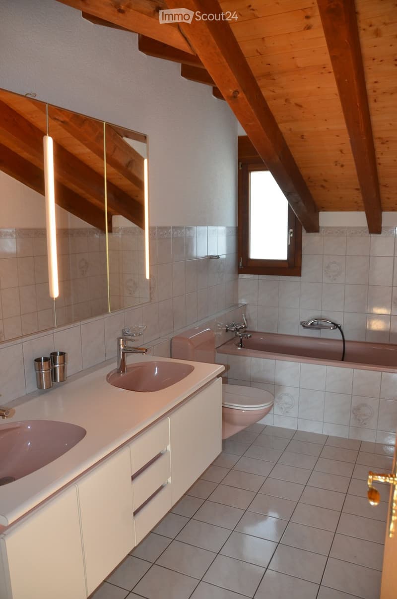Bathroom with double sink, toilet, bathtub, and a large mirror. The room has wooden beams on the ceiling and a window letting in natural light.