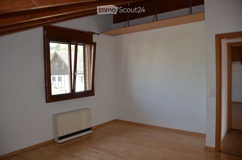Empty room with wooden flooring, white walls, a window with wooden frame, a radiator, and a doorway leading to another space.