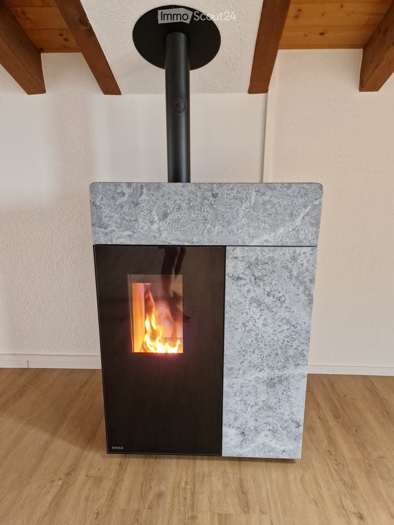 Modern fireplace with a sleek black chimney and a concrete base, featuring a glowing fire inside.