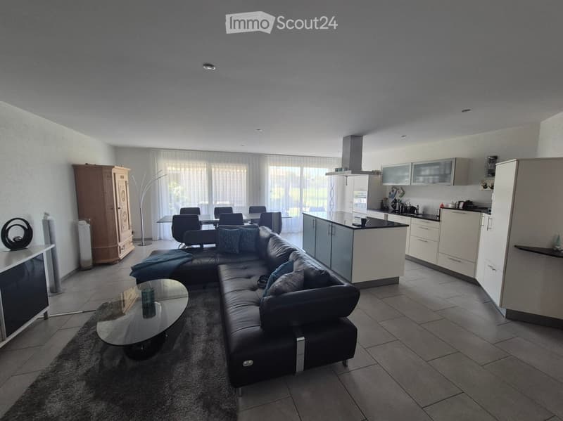 Open-plan living and dining area with a black leather sofa, glass coffee table, dining table with chairs, and a modern kitchen with white cabinets and stainless steel appliances.