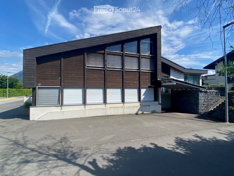 Modern two-story house with dark wooden facade, large windows, and raised ground floor.