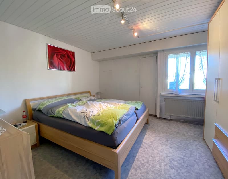 Compact room with a lofted bed, white walls, wooden flooring, and a picture of a rose on the wall.
