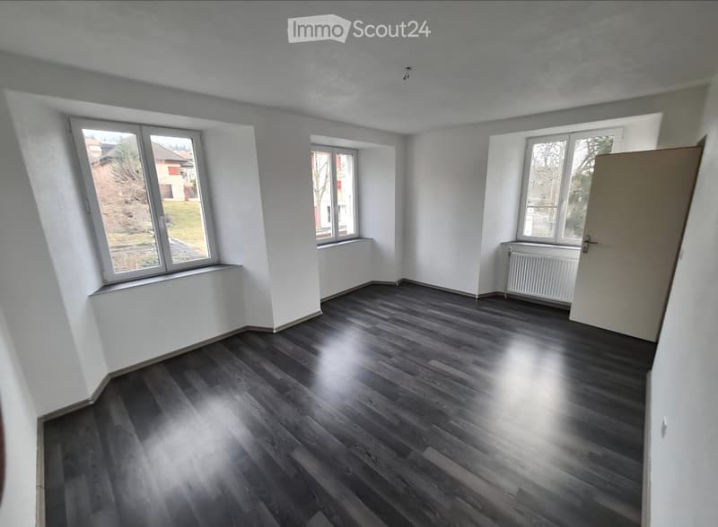 Empty room with dark wooden flooring, white walls, and multiple windows offering natural light. No furniture or equipment is present.