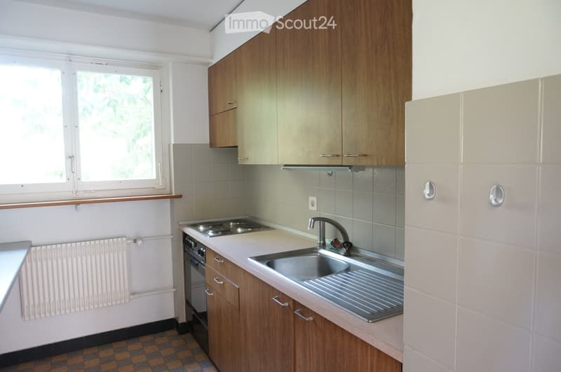 Modern kitchen with wooden cabinets, stainless steel sink, stove, and oven. Light-colored tiles and a window provide natural light.
