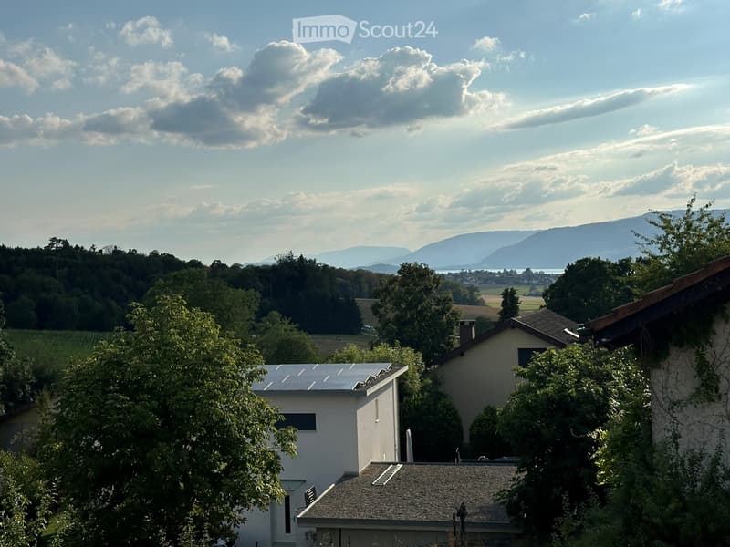 View of a residential area with houses, trees, and distant mountains under a partly cloudy sky.