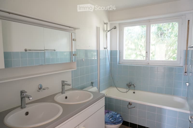 Bathroom with double sink, bathtub, mirror, and window with view of greenery.