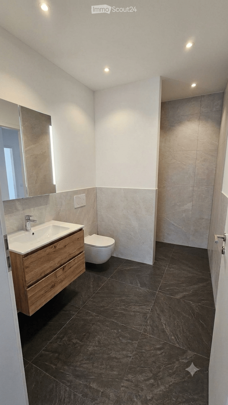 Modern bathroom with dark marble tiles, a wooden sink cabinet, a toilet, and a large mirror.
