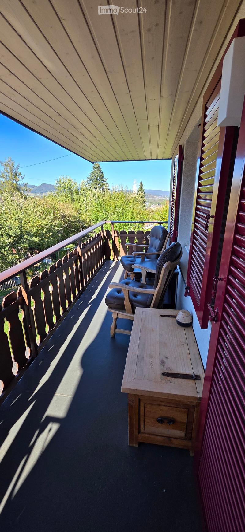 Balcony with wooden chairs, small table, and scenic mountain view.