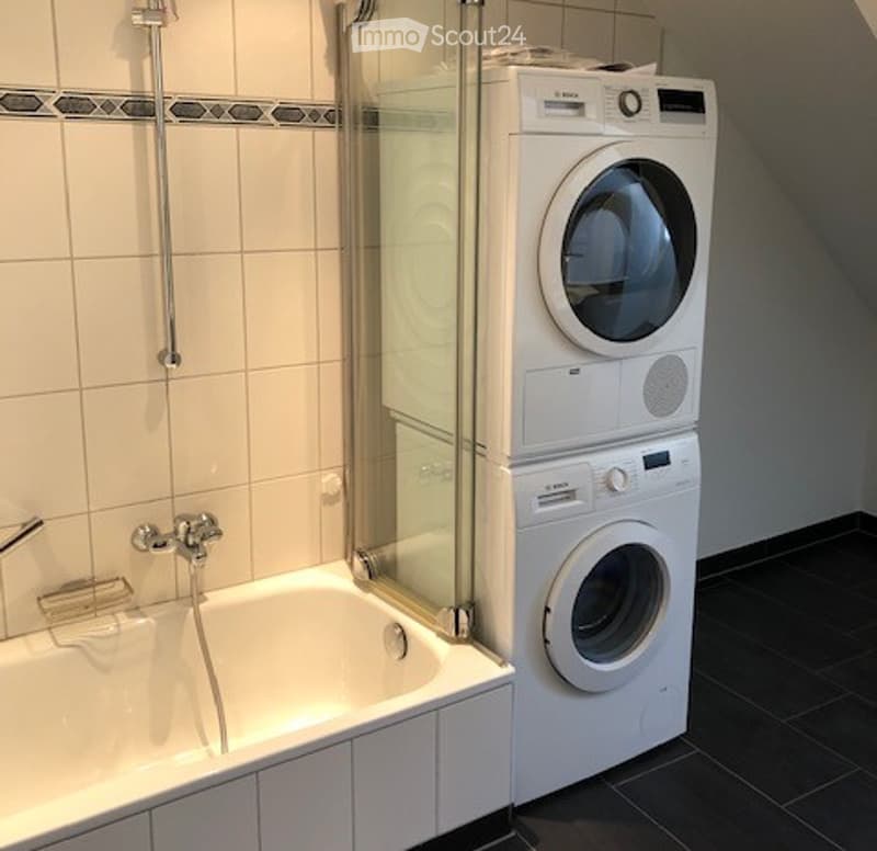 Modern bathroom with a bathtub, shower, and stacked washing machine and dryer unit.