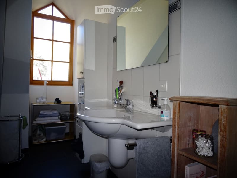 Bathroom with a white sink, mirror, cabinet, and various toiletries. Features a window with wooden frame and a towel hanging on the side.