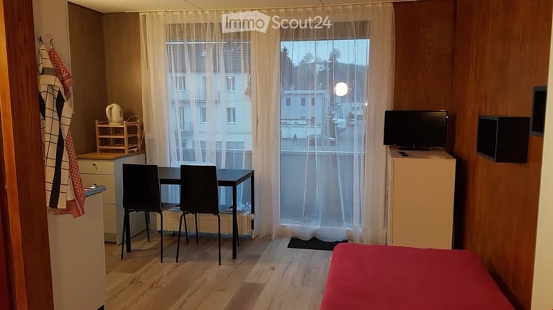 small room with a desk, chair, and bed, window with curtain, television, cabinet, floor radiator