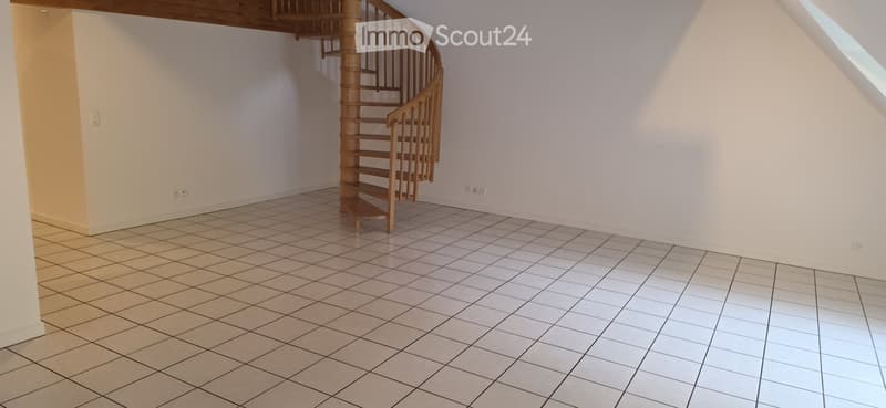 Empty room with tiled floor and a wooden spiral staircase leading upwards.