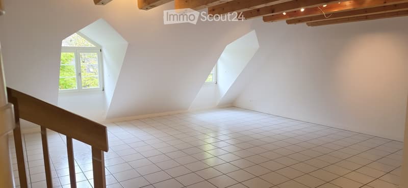 Empty attic room with white tiled floor, white walls, exposed wooden beams, and two skylight windows.