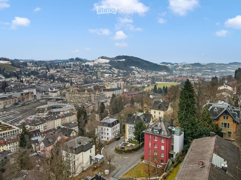 Aerial view of a city with diverse buildings, mountains, and a clear sky.
